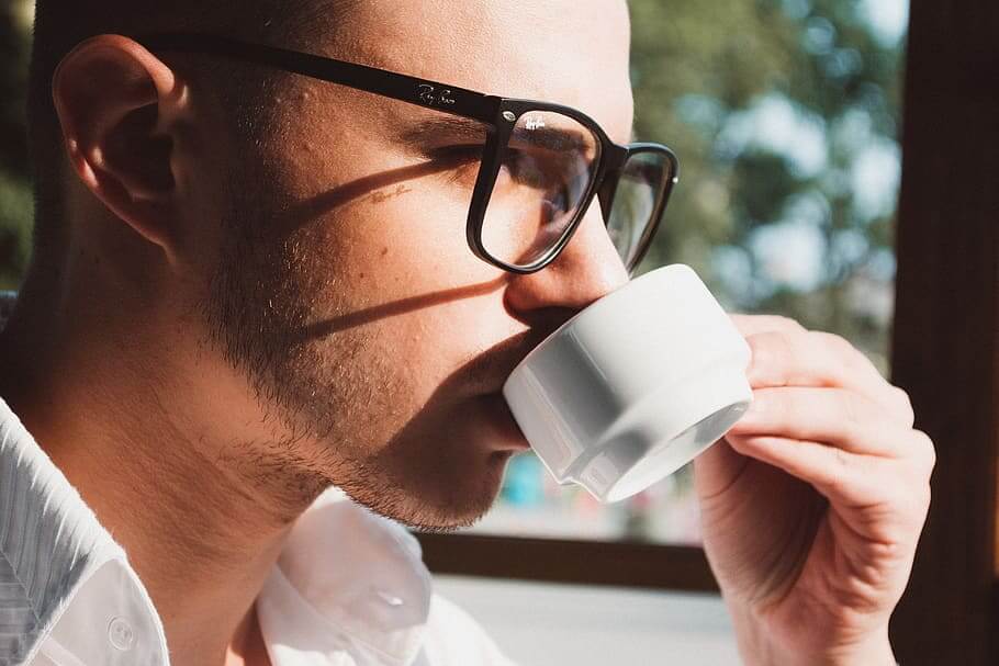 Một người đàn ông đeo kính đang uống cà phê